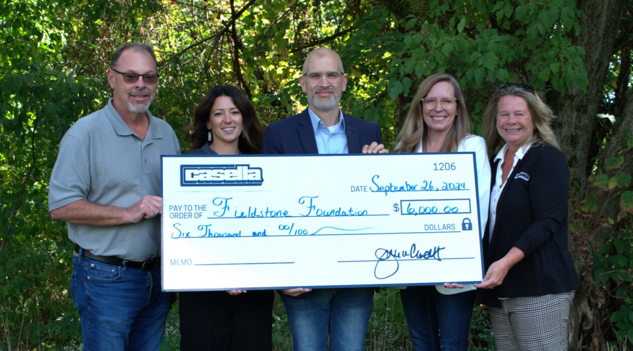 Five people stand together holding a large check for $6,000, representing a donation from Casella Waste Systems to the Fieldstone Foundation. Smiling, they pose in front of a simple backdrop, with the check prominently displaying the amount and donor information.